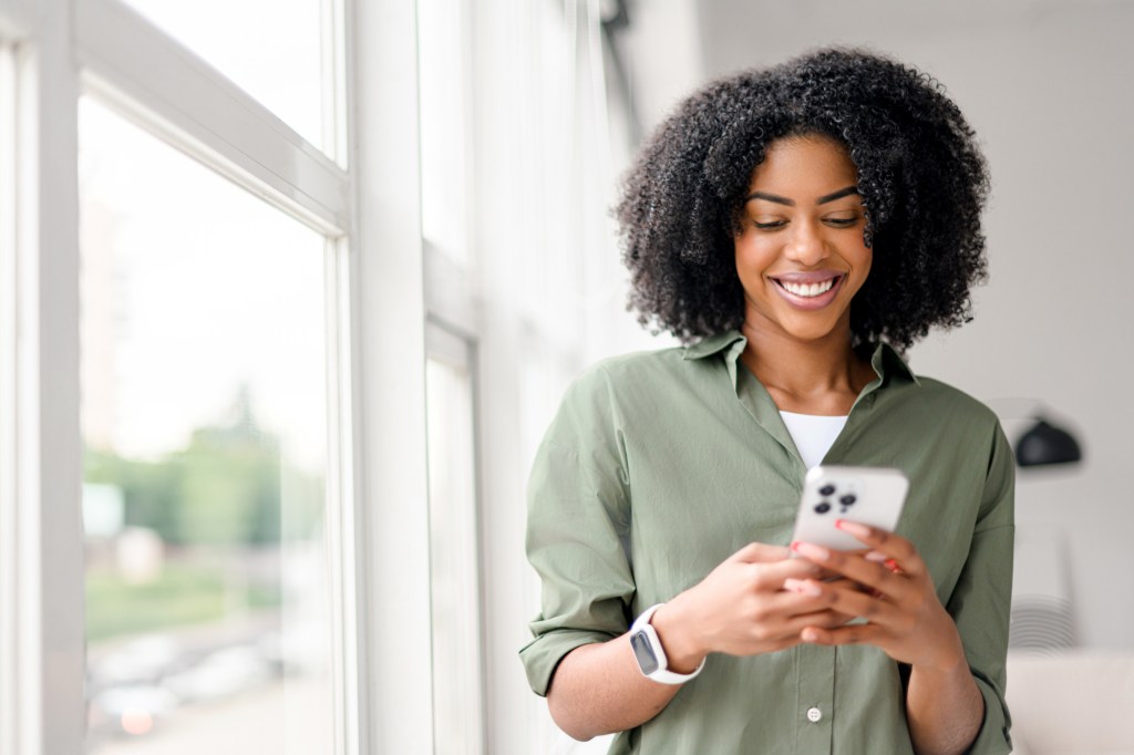 An African-American woman with a contagious smile interacts with her smartphone